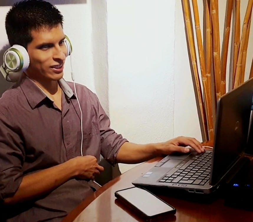 Una persona ciega frente a su computadora portátil, escucha el lector de pantalla a través de audífonos